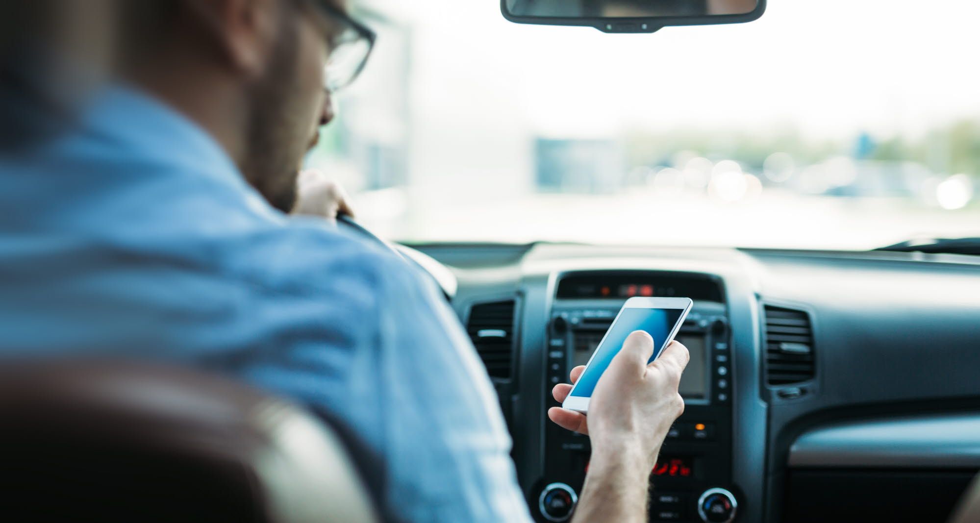 man driving while looking at mobile